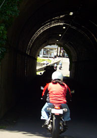 最後の短いトンネルを抜けると、目の前に常神の漁港と集落、そして集落に覆いかぶさるような半島先端の山が見える。 最後の短いトンネルを抜けると、目の前に常神の漁港と集落、そして集落に覆いかぶさるような半島先端の山が見える。